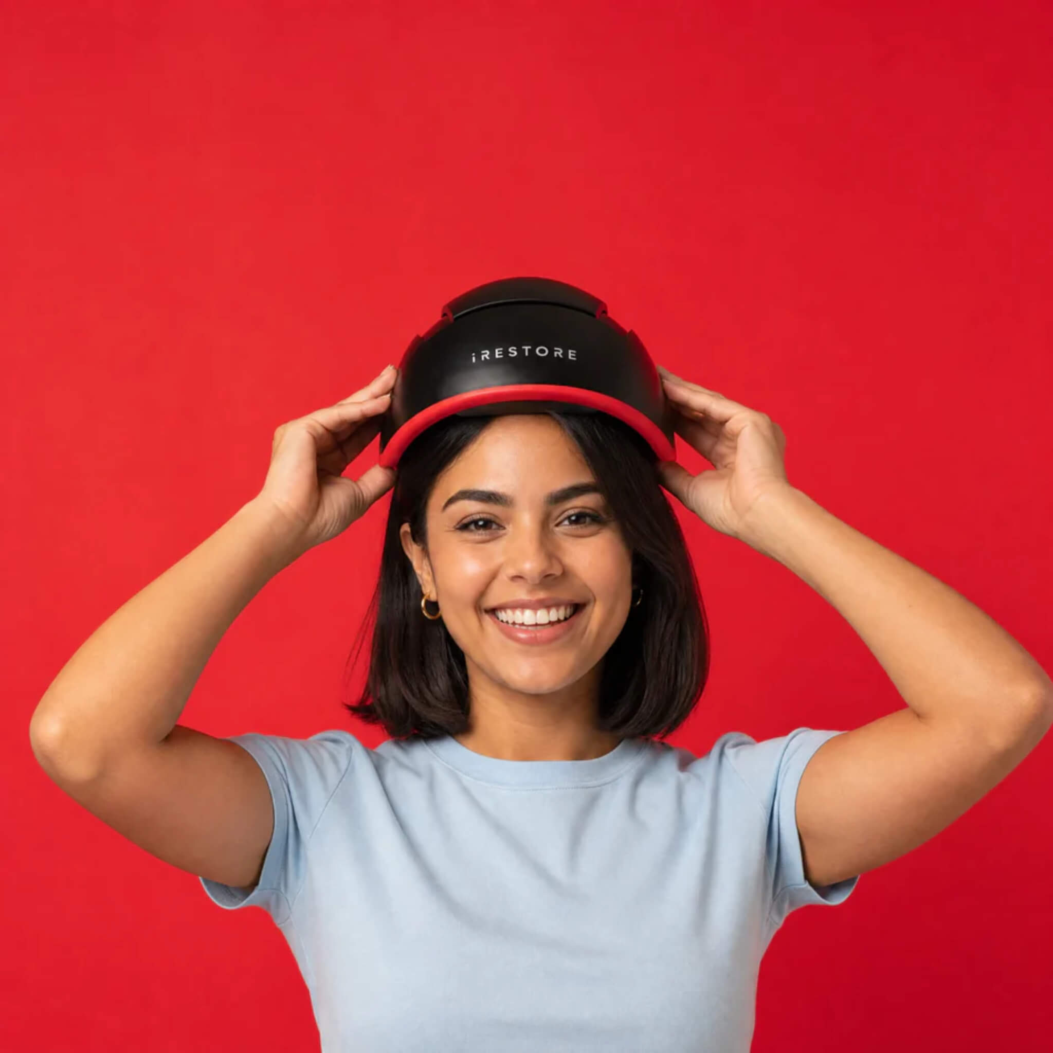 Woman putting on iRESTORE Elite laser hair growth helmet showing easy hands-free daily use