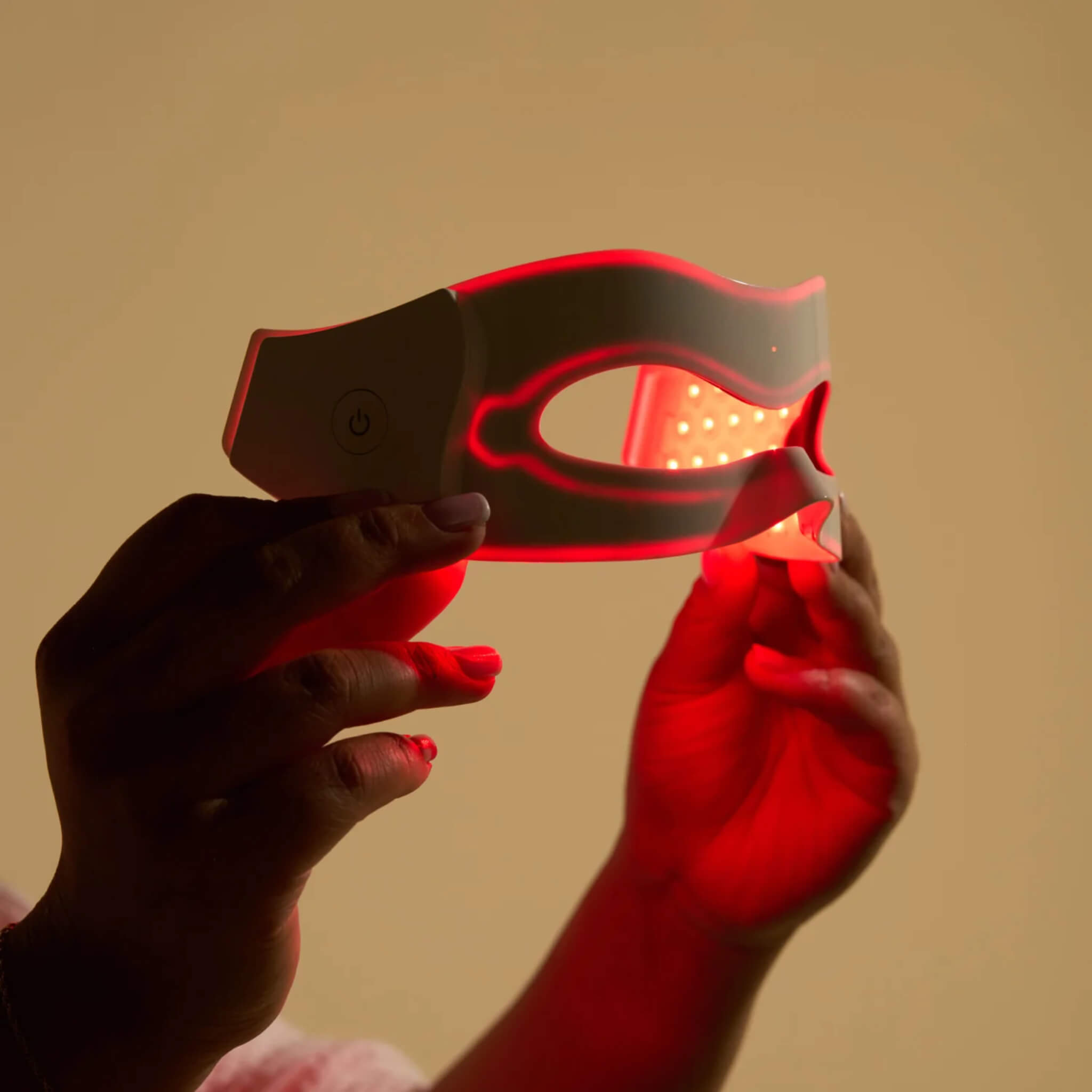 Hands holding the iRESTORE Illumina Eye Mask showing red LED light illuminated