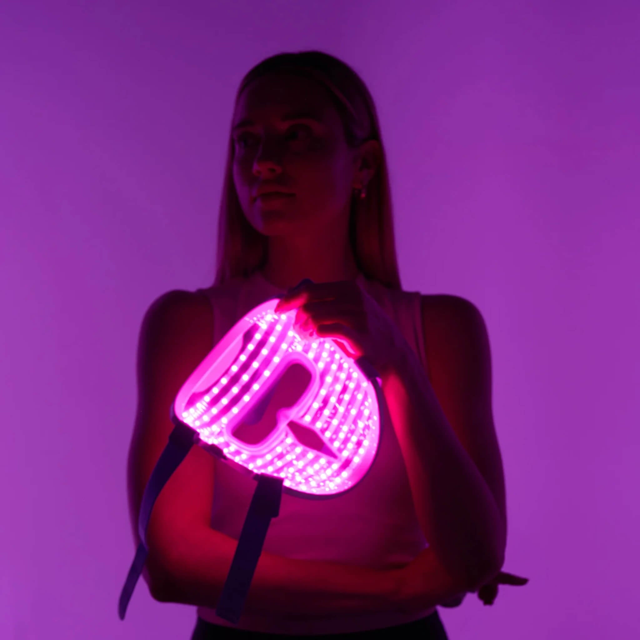 Woman holding the iRESTORE Illumina face mask illuminated in infrared light mode