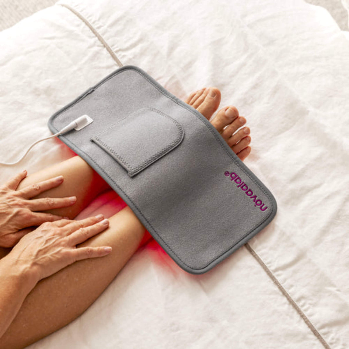 NovaaLab Novaa Light Pad resting over a woman’s feet on a bed with red light glowing underneath