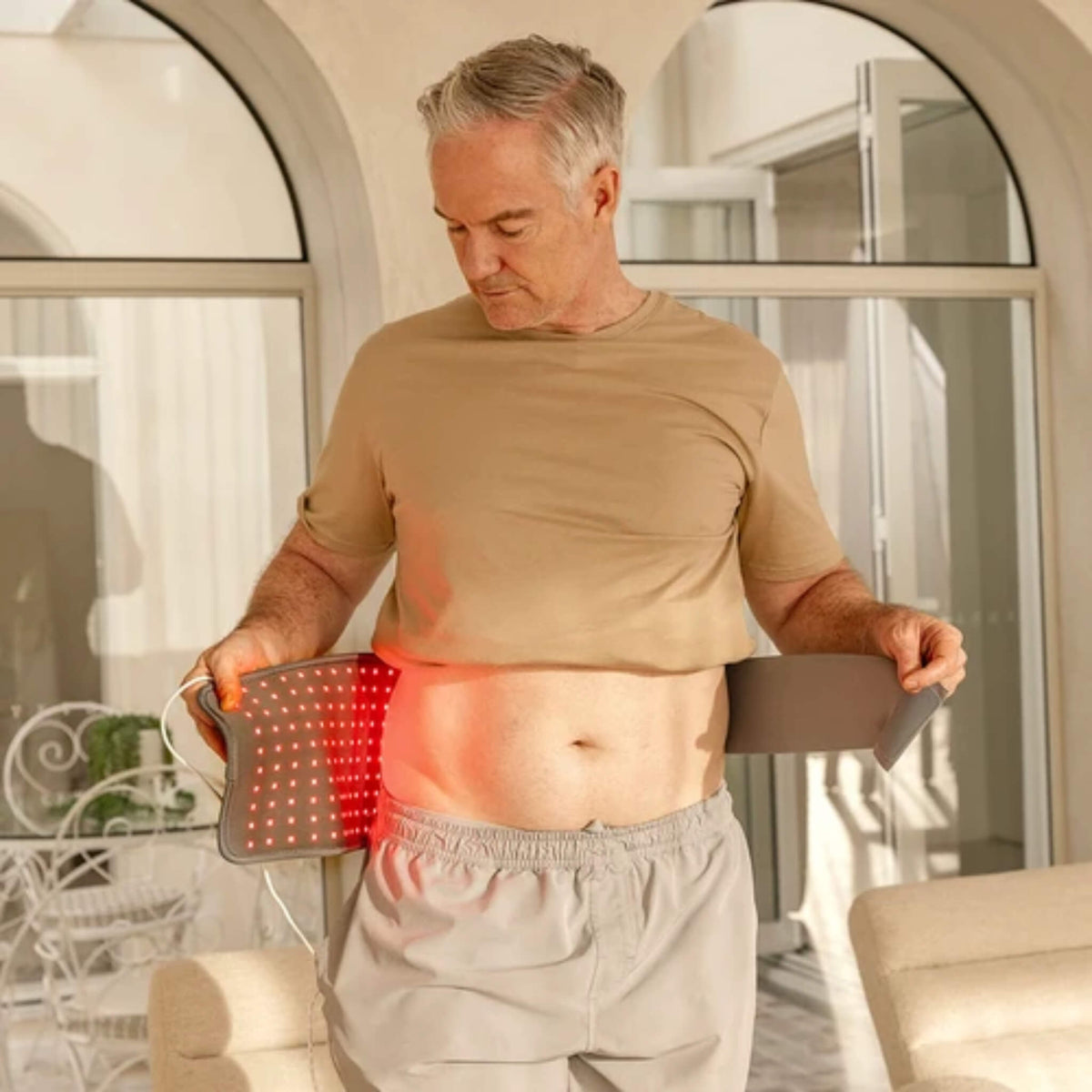 Man wrapping the NovaaLab Novaa Light Pad around his waist with the stretchy strap and the red LEDs lit
