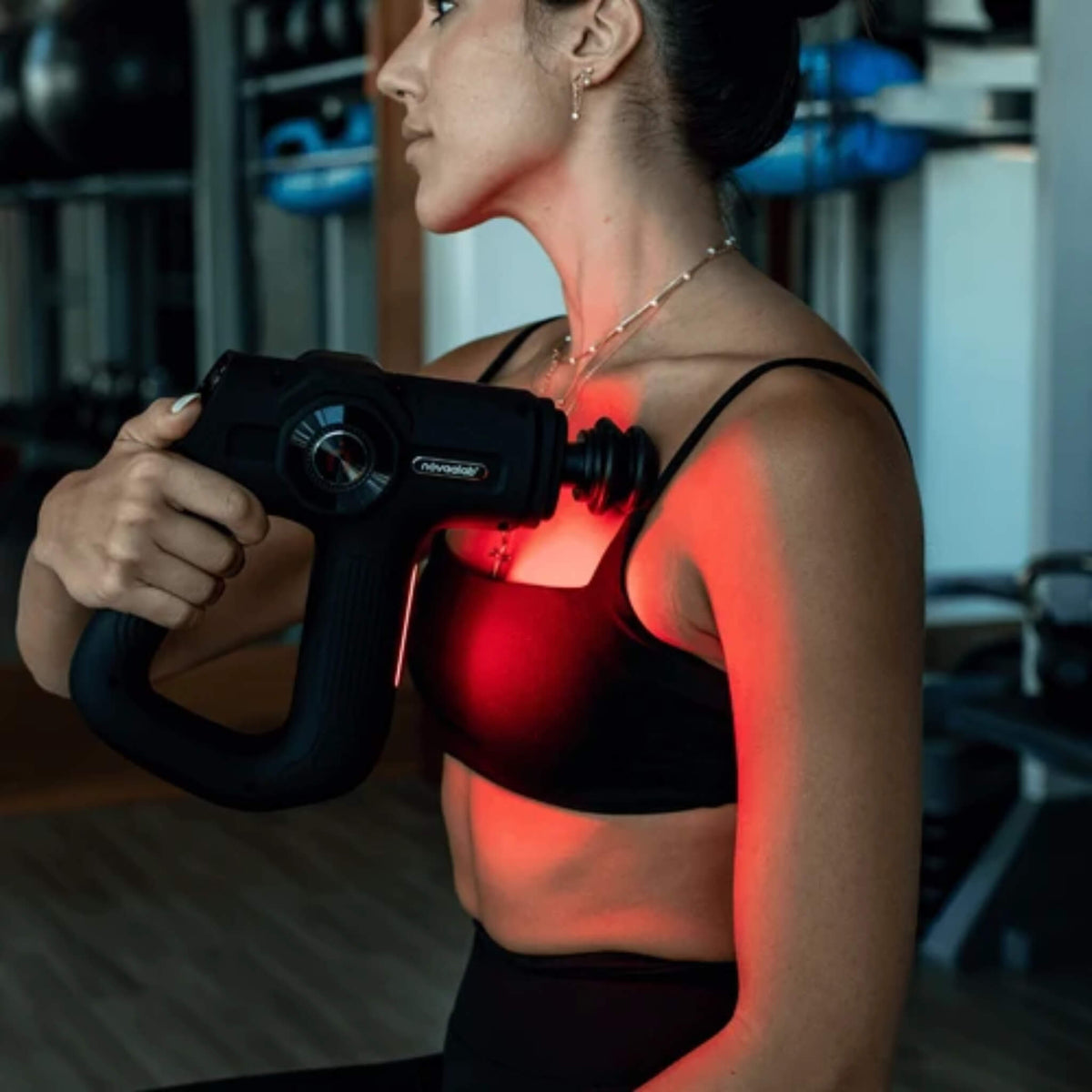 NovaaLab Novaa Pulse R percussion massage gun with red light in use on the front of a woman’s shoulder