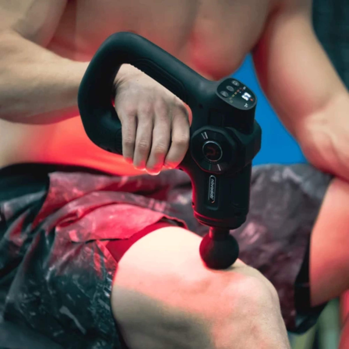 Man using the NovaaLab Novaa Pulse R percussion massage gun with the round head on his thigh