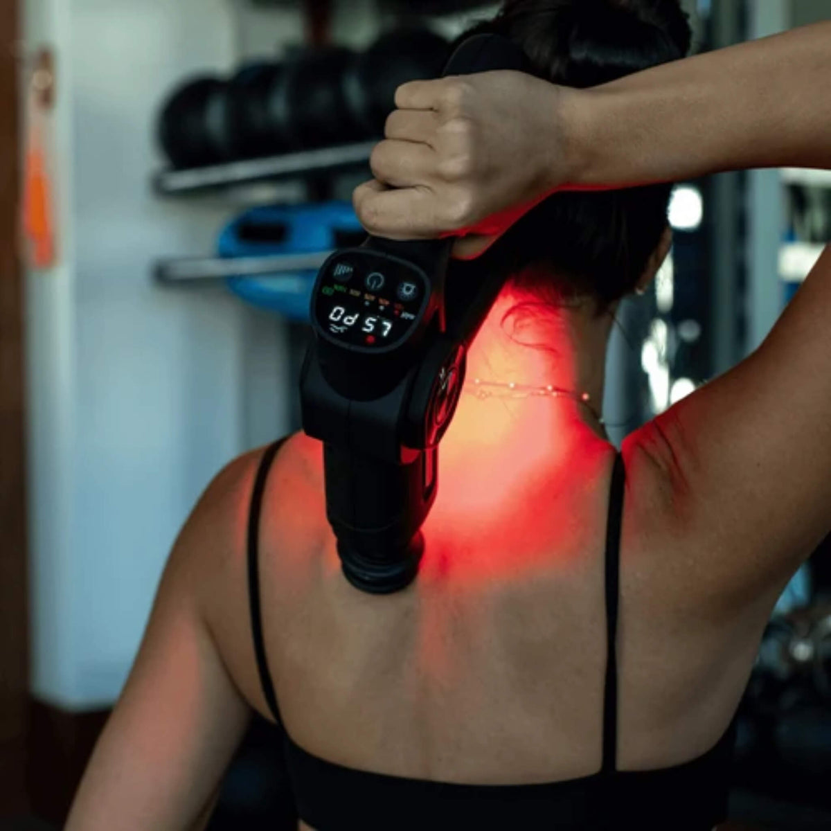NovaaLab Novaa Pulse R percussion massage gun in use on a woman’s upper back with the display and red light visible