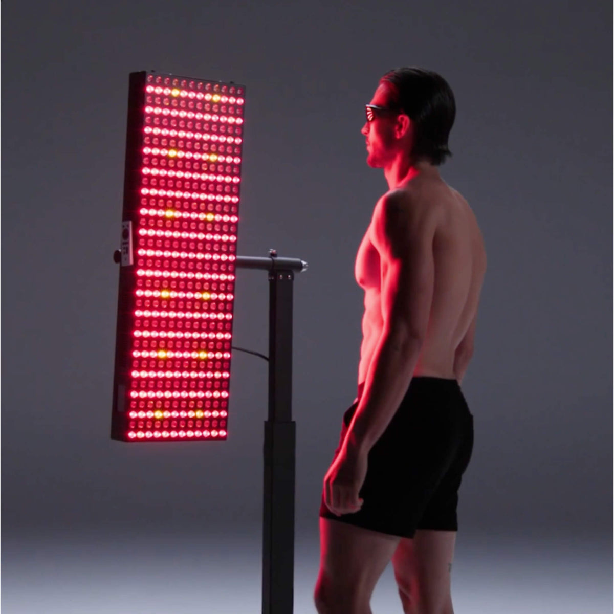 Man wearing protective glasses standing beside the iRESTORE Apex Elite 2160 full body red light panel with all LEDs lit red