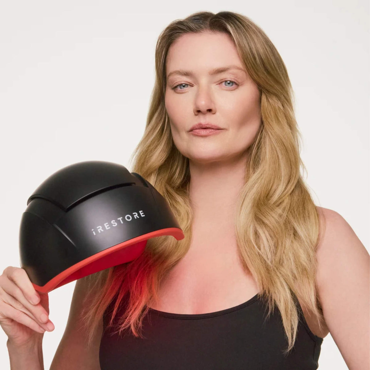 Woman holding the iRESTORE Elite Hair Growth System helmet beside her