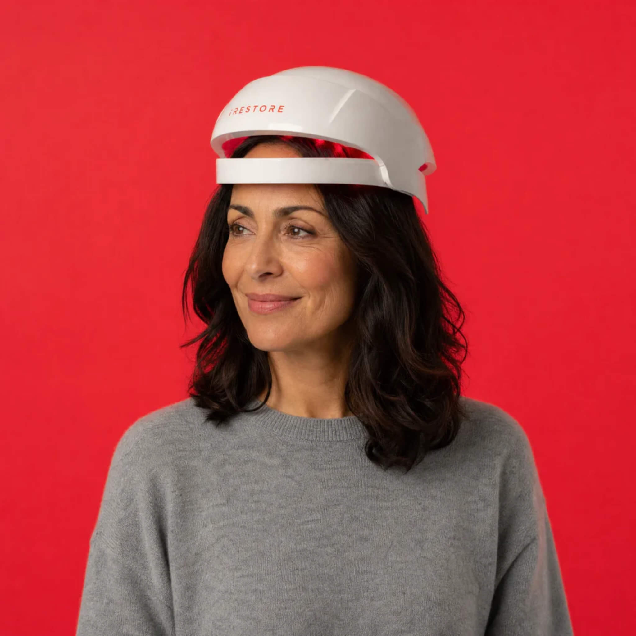Woman wearing iRESTORE Essential laser hair growth cap in gray sweater