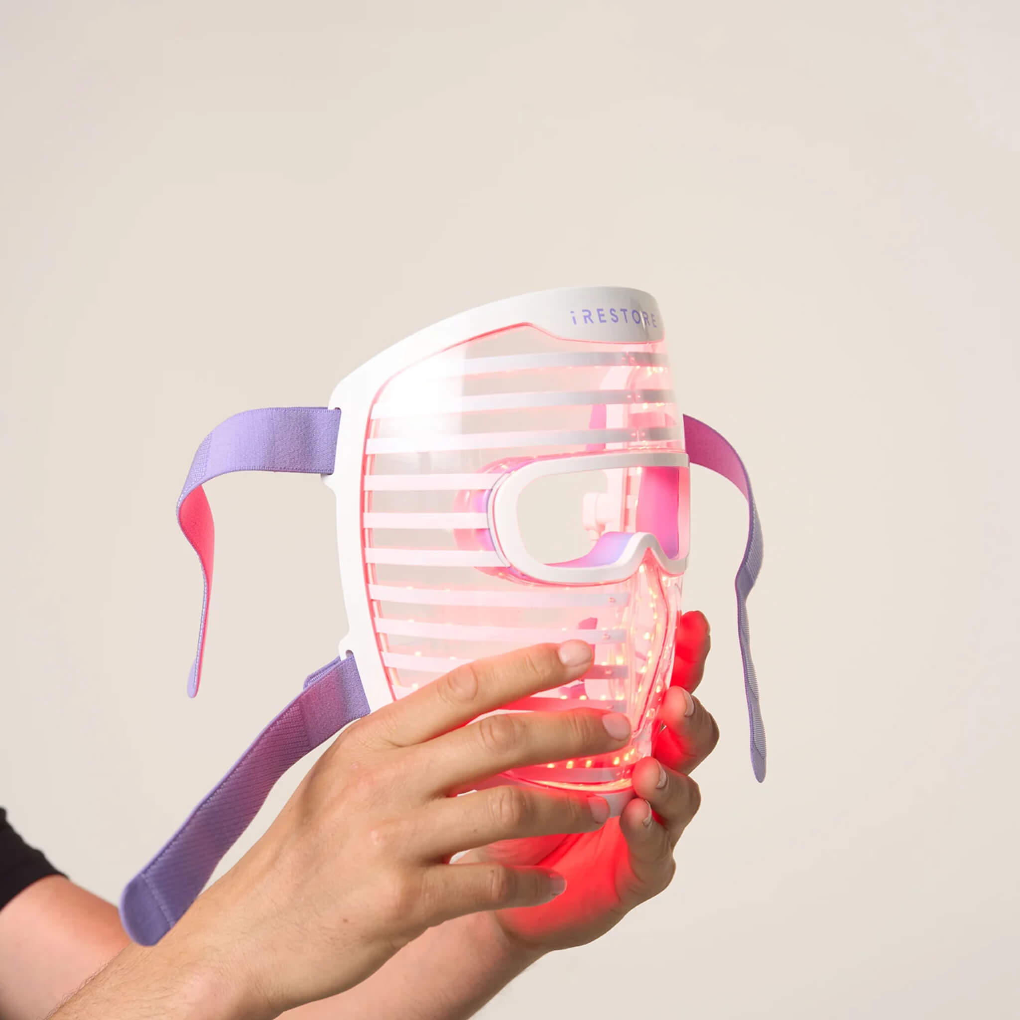 Hands holding the iRESTORE Illumina face mask showing red LED light illuminated