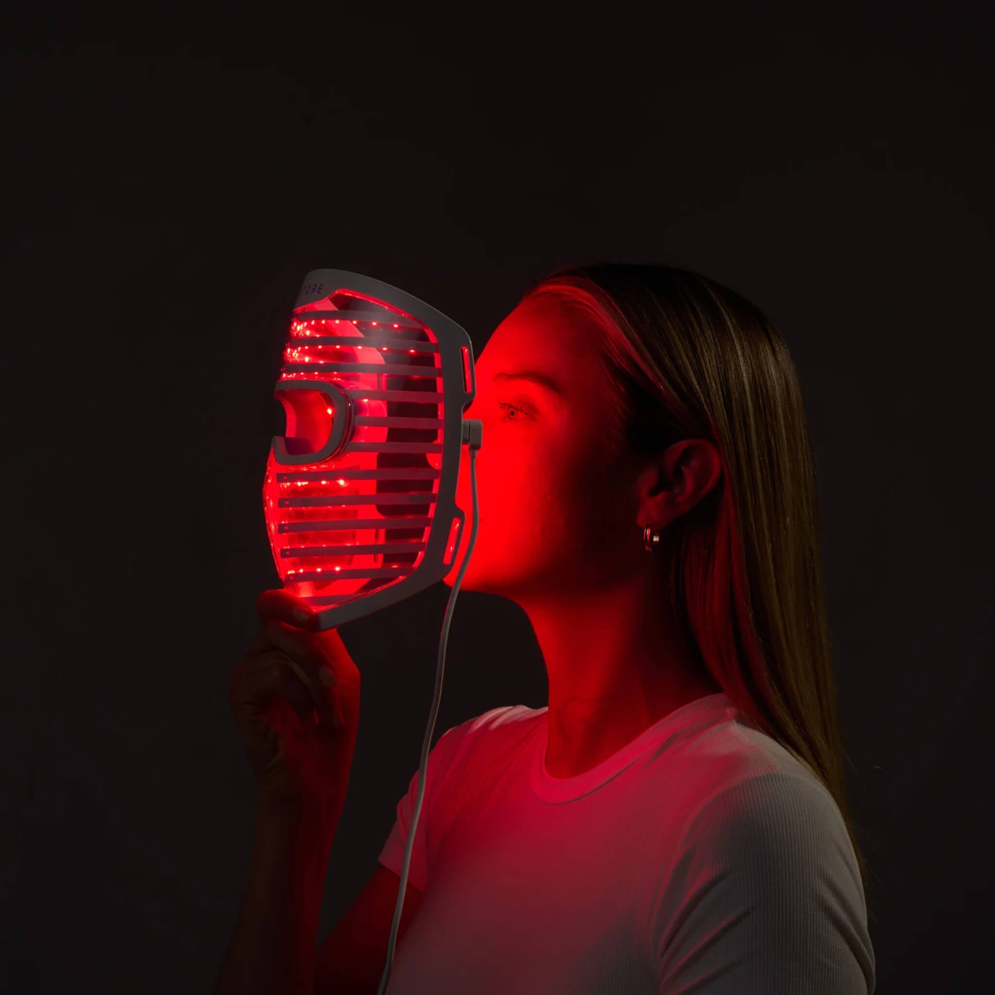Woman using the iRESTORE Illumina face mask in red light therapy mode