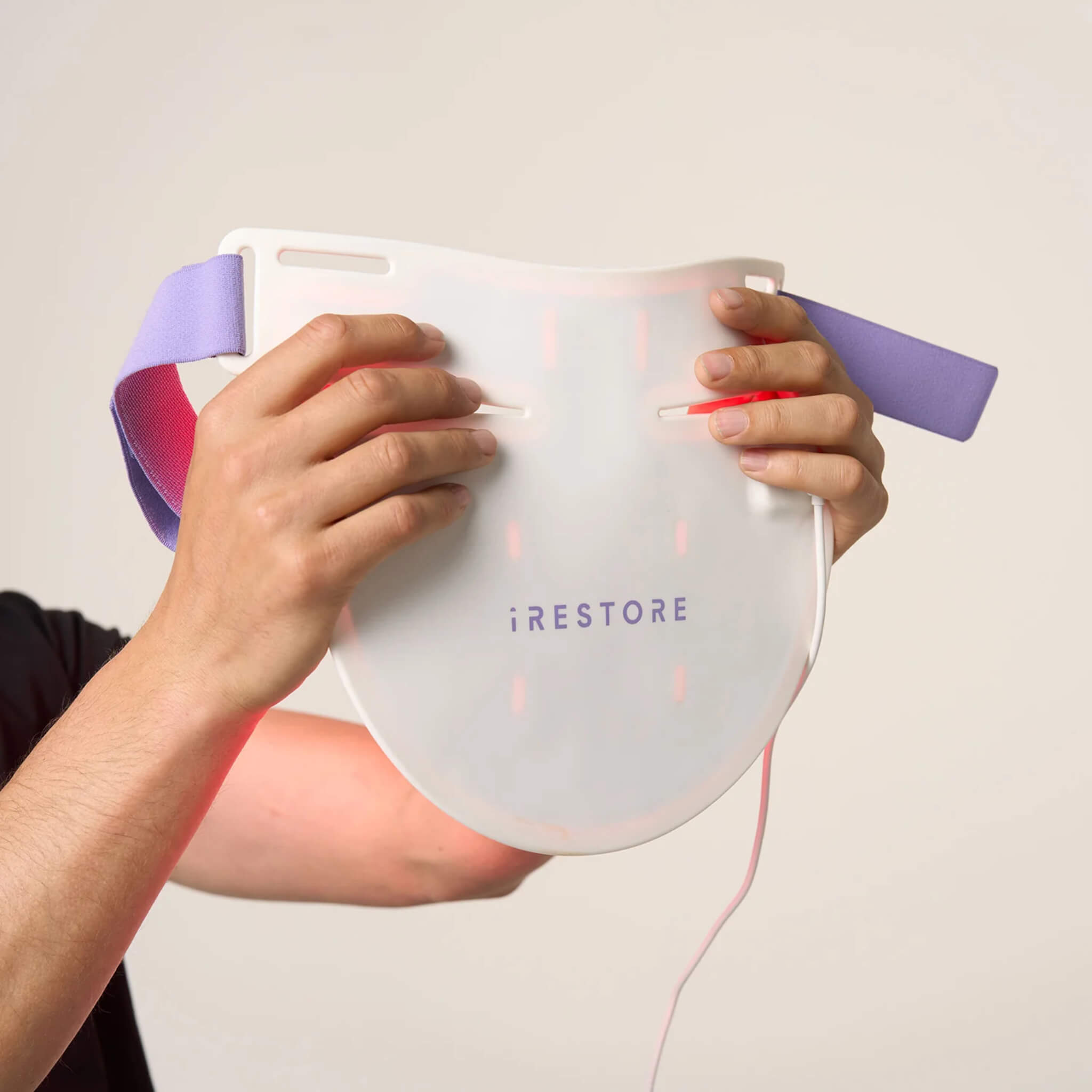 Hands holding the iRESTORE Illumina Neck & Chest Mask showing red light illuminated
