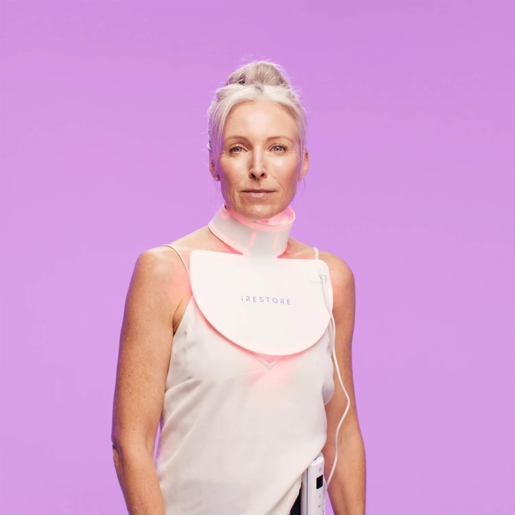 Mature woman wearing the iRESTORE Illumina Neck & Chest Mask against a purple background