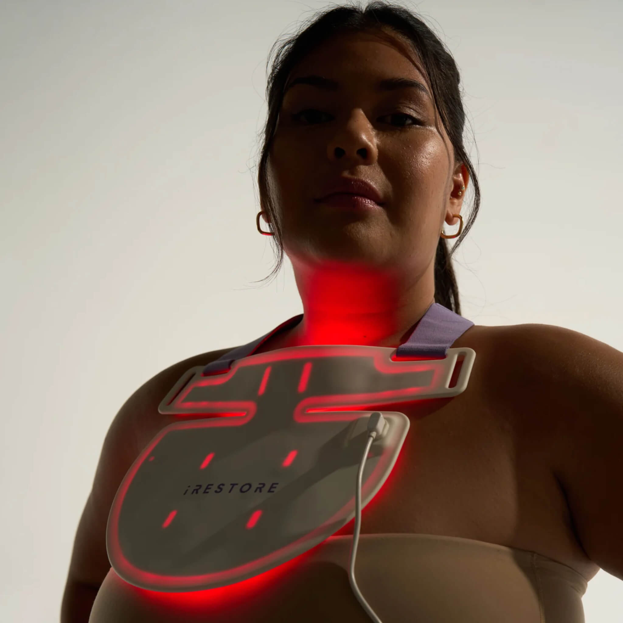 Close-up of woman wearing the iRESTORE Illumina Neck & Chest Mask illuminated in red light