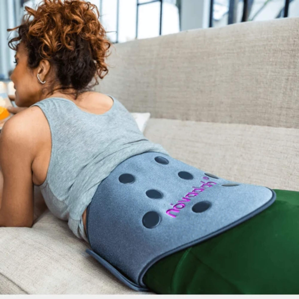 Woman relaxing on a couch wearing the NovaaLab Novaa Back Pad on her lower back