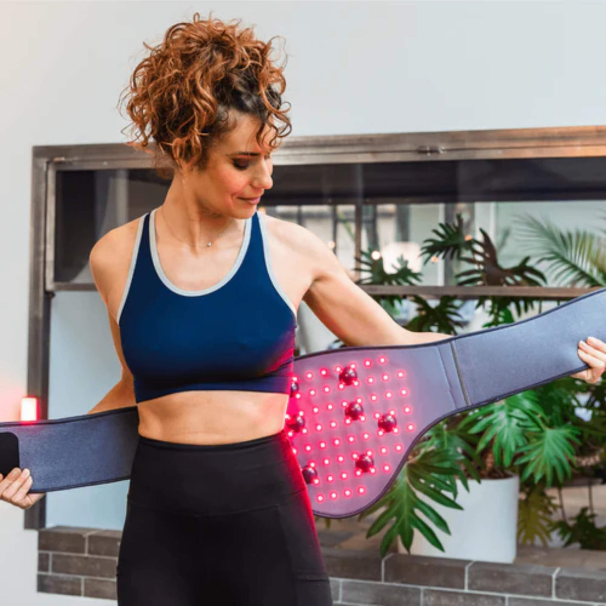 Woman wrapping the NovaaLab Novaa Back Pad around her waist with the red LEDs and vibration points lit