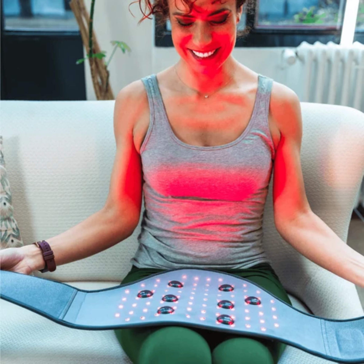 Woman seated holding the NovaaLab Novaa Back Pad open with its red LEDs and 8 vibration points lit