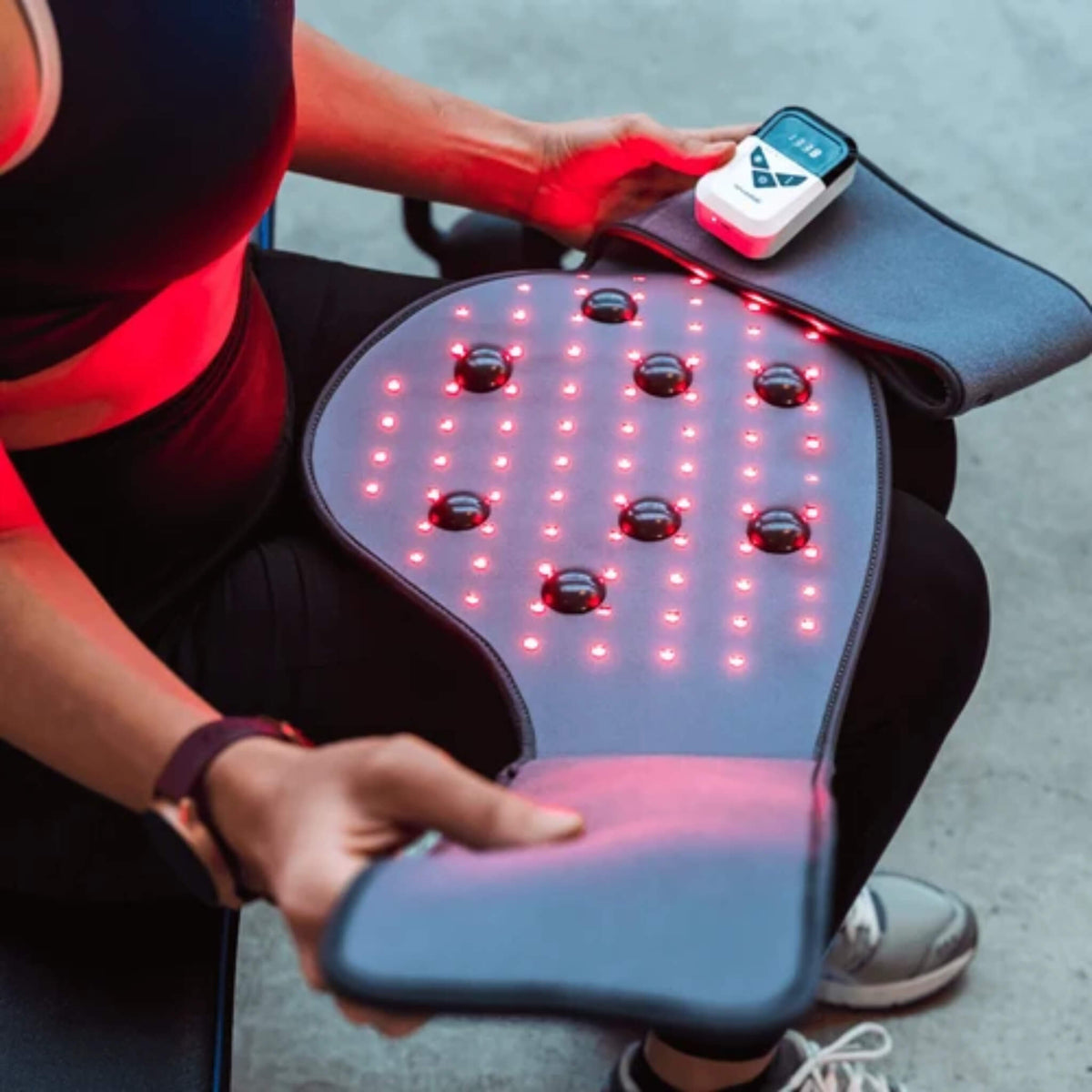 NovaaLab Novaa Back Pad lit with red LEDs on a lap, with the portable battery remote attached to the wrap
