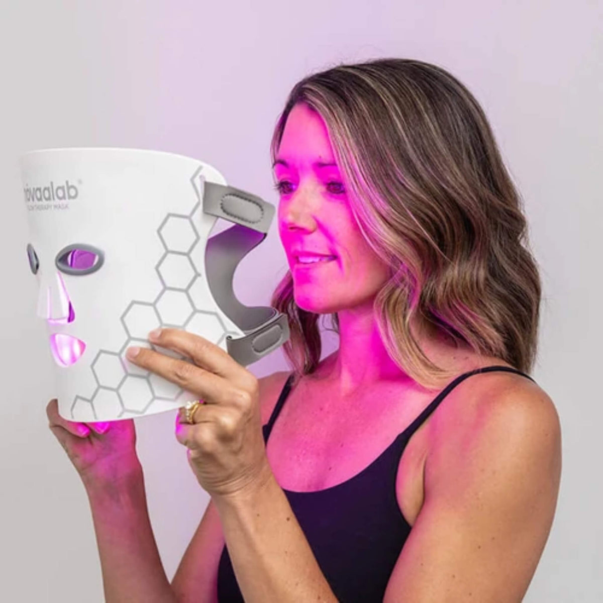 Woman holding the NovaaLab Novaa Glow Therapy Mask glowing in purple light mode