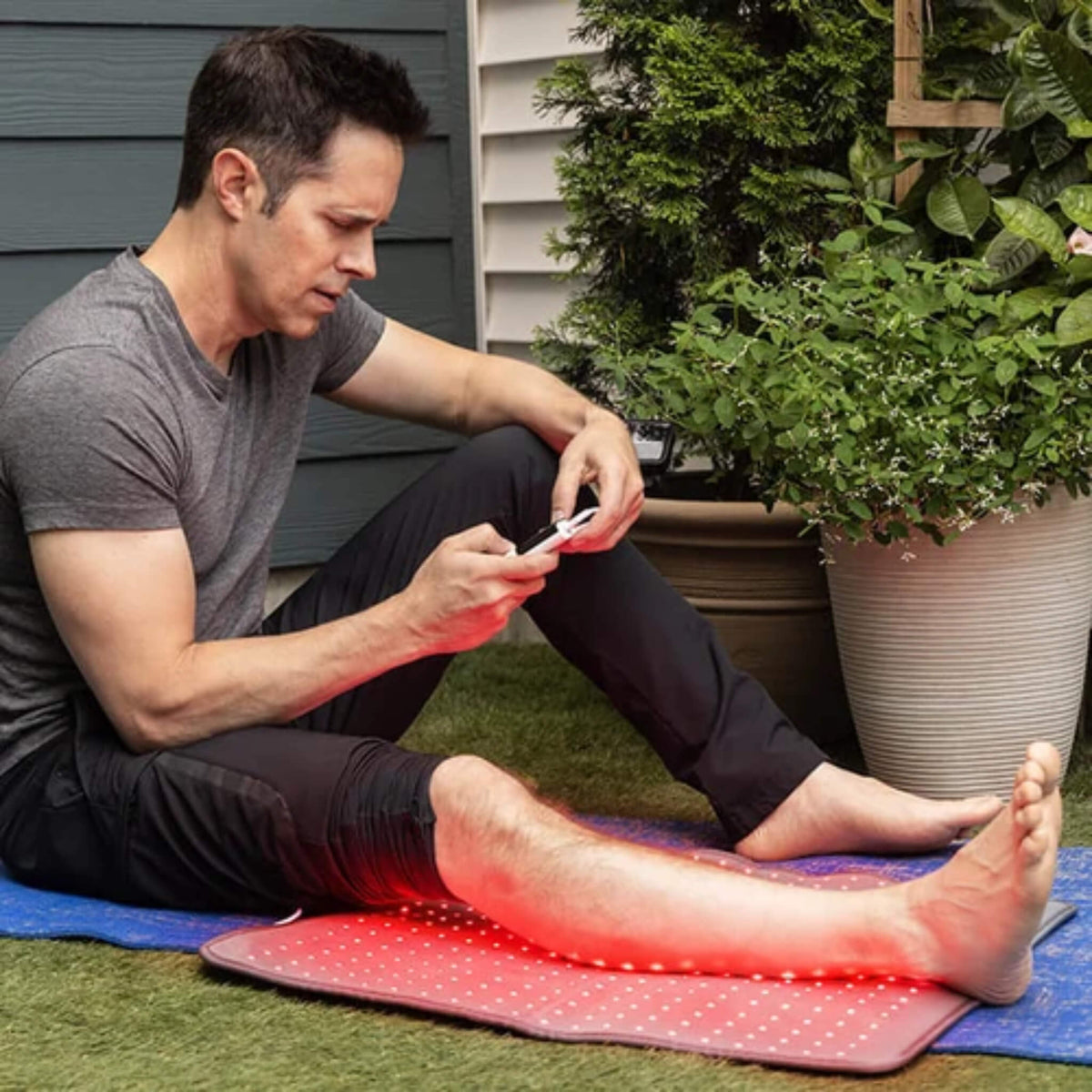 Man resting his legs on the NovaaLab Novaa Light Pad XL while adjusting the remote