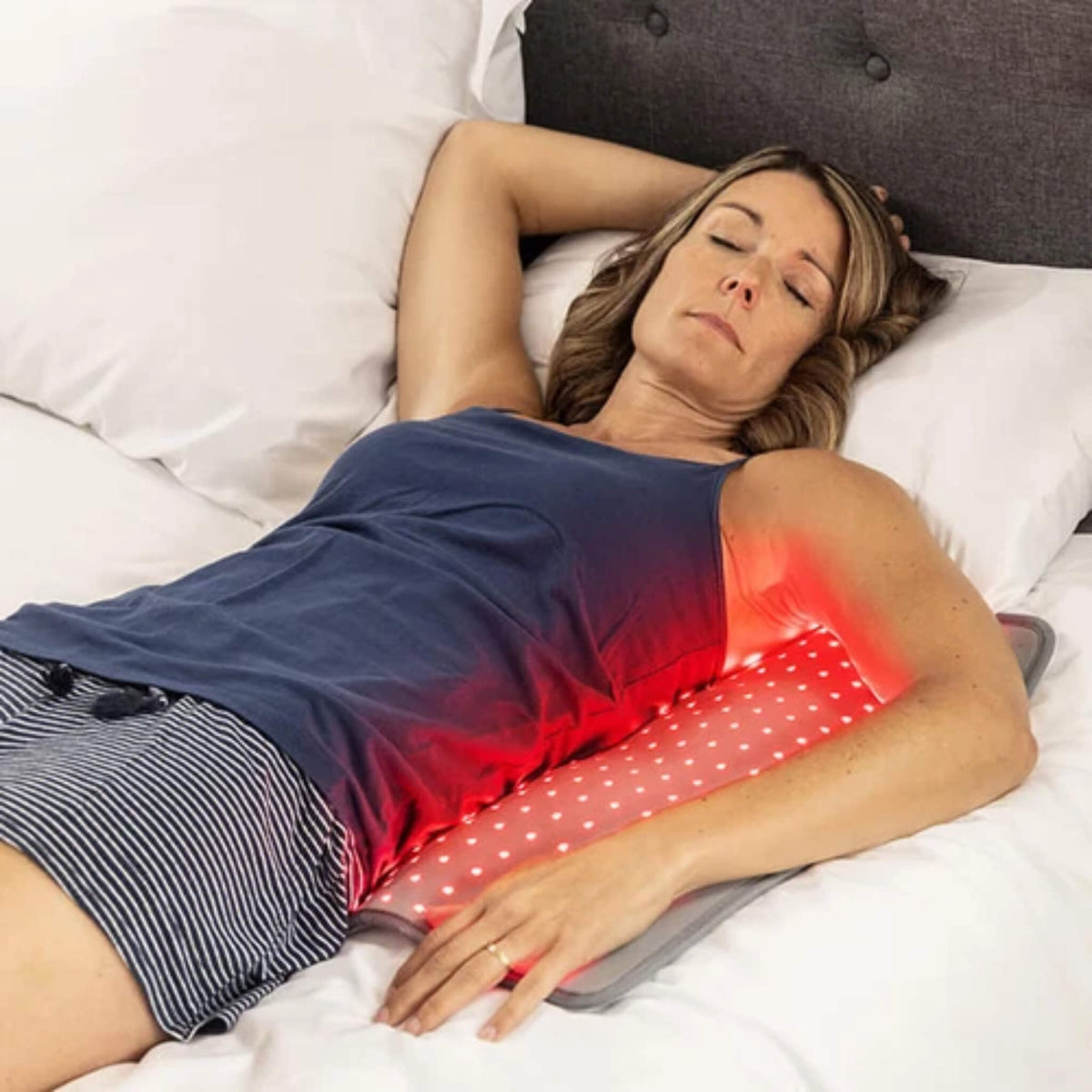 Woman lying in bed on the NovaaLab Novaa Light Pad XL during a session