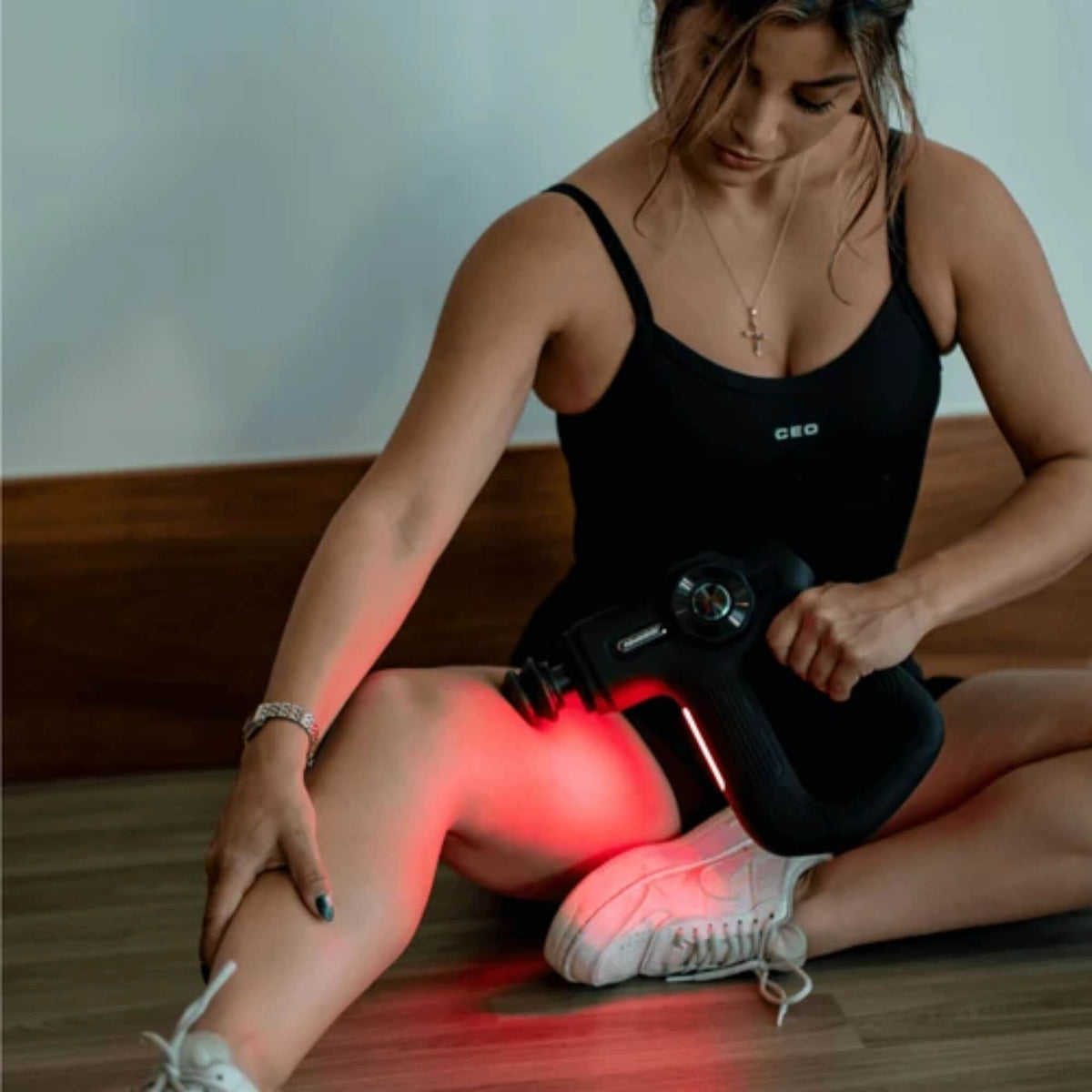 Woman seated on the floor using the NovaaLab Novaa Pulse R percussion massage gun on her leg