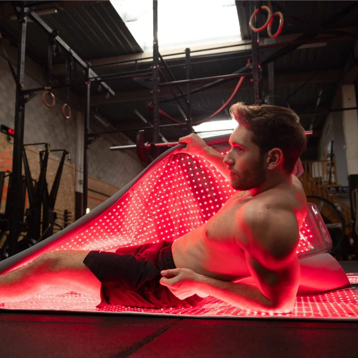 Man in a gym lifting the upper half of the NovaaLab Novaa Recovery Pod with the red LEDs lit