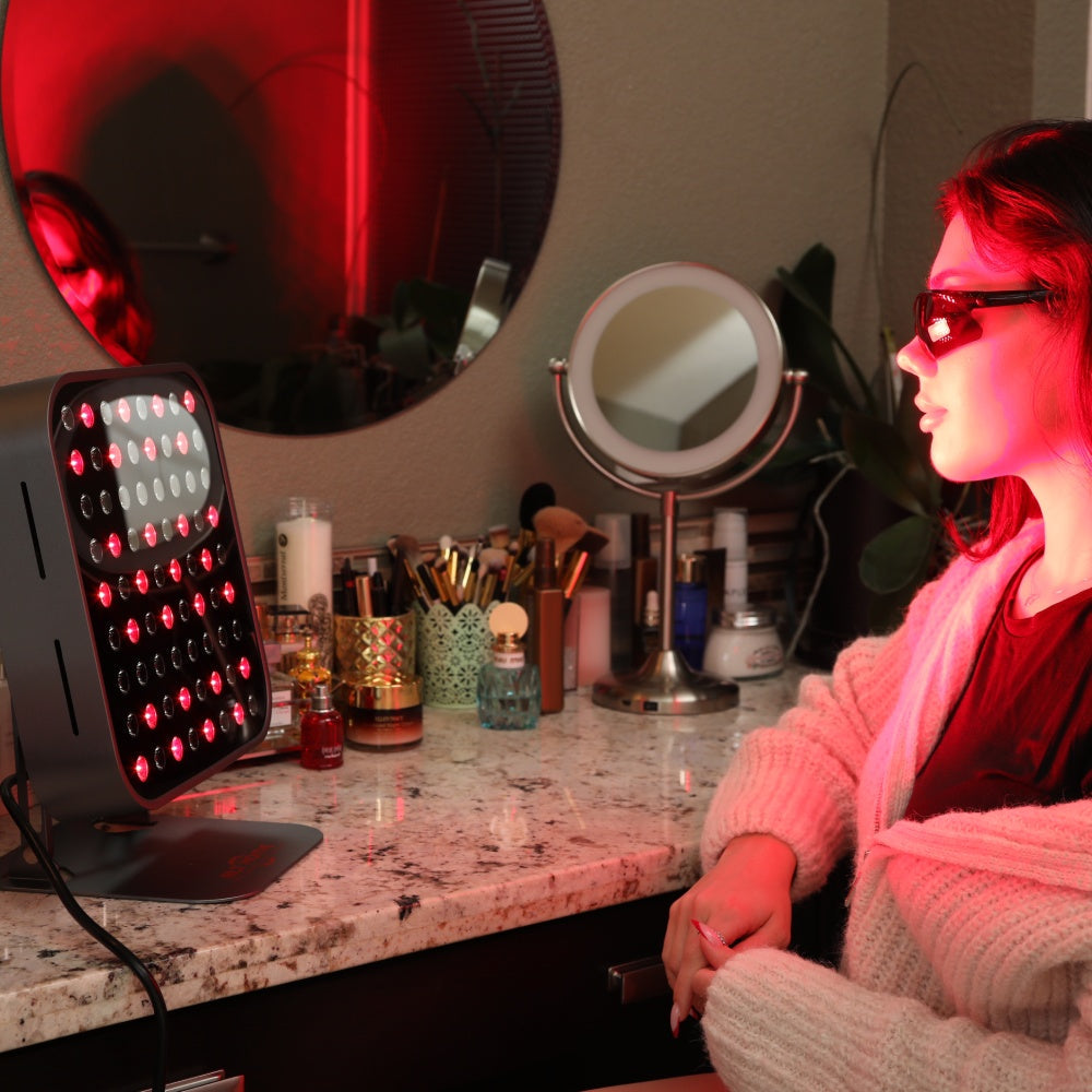 Woman wearing eye protection at a vanity using the RLT Home Total Spectrum MINI Red Light Therapy Device